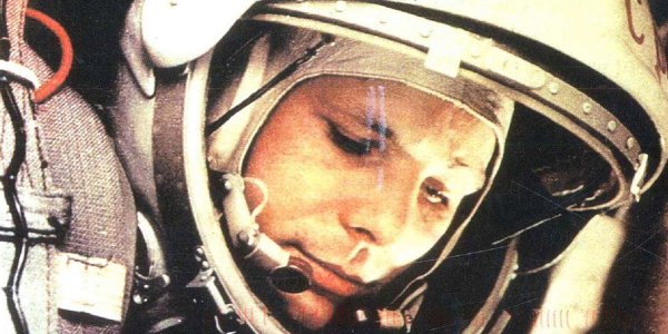 Photo de Gagarine dans sa combinaison spatiale, trouvée sur Wikimédia Commons. On voit un gros plan sur son visage regardant vers le bas de l'image, avec un demi-sourire, il porte une sorte de capuche à l'intérieur d'un casque dont la visière semble relevée et sur lequel on devine en haut « CCCP ». On voit un peu de matériel autour mais sans vraiment pouvoir dire ce dont il s'agit, le Vostok était équipé de pas mal de capteurs pour vérifier l'état de santé de son passager.