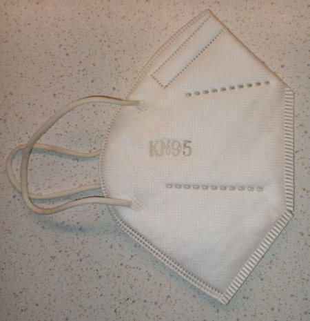 Photo, trouvée sur Wikimédia Commons, d'un masque FFP2, un outil efficace pour réduire les risques de contamination aéroportée (en plus de protéger aussi des particules fines quand il y a un incendie à proximité, ce qui peut aussi être assez utile par les temps qui courent). Le masque est ici simplement présenté plié en deux et posé devant nous, avec la partie qui doit couvrir le visage du haut du nez au bas du menton (on voit la marque de la partie rigide qui le fait tenir sur le nez), des élastiques pour le faire tenir aux oreilles (ce qui n'est pas le plus agréables, les masques tenant sur l'arrière de la tête le sont beaucoup plus) et la mention « KN95 », qui si j'ai bien compris est environ l'équivalent de « FFP2 » avec les normes chinoises.