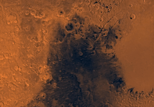 Assemblage de photographies réalisées par l'orbiteur de Viking 1, dont on reparlera plus bas, et trouvée sur la page Wikipédia dédiée à Syrtis Major Planum, un haut plateau volcanique martien (le Syrtis Major, comme les autres volcans de Mars, étant aujourd'hui éteint). On voit donc une « vue aérienne » du sol de Mars, majoritairement marron et avec une multitude de cratères d'impact, mais une grande zone au centre et au bas de l'image est visiblement beaucoup plus sombre et comporte moins de cratères. La différence de couleurs est essentiellement due à la composition des roches. Cette zone représente d'ailleurs l'extrémité d'une grande région volcanique qui a été la première zone géographique identifiée à la surface de Mars en raison de sa différence de couleur avec le reste, on en reparlera plus bas.