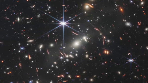 Premier champ profond (ou « deep field » en anglais) réalisé par le télescope spatial James Webb. On voit quatre étoiles reconnaissables aux six rayons lumineux autour d'elles (il s'agit d'un artefact dû au télescope, ces rayons n'existent pas dans la réalité) et tout le reste des taches lumineuses visibles sur cette image sont des galaxies, dont la plupart sont particulièrement lointaines. Elles ont plusieurs couleurs distinctes, globalement du jaune au rouge, en fonction de leur éloignement, mais on verra ce point plus en détails dans un prochain thread.