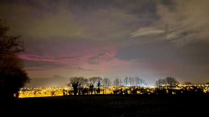 Autre photo prise par mon collègue un peu plus loin de la maison des deux précédentes. On voit cette fois une rangée d'arbres dans l'obscurité du premier plan, mais qui est loin de cacher les lampadaires allumés situés derrière, formant une bande de lumière quasi-continue. Avec tous ces lampadaires, le ciel est également beaucoup plus lumineux, ce qui rend les lueurs des aurores beaucoup plus pâles et plus difficiles à discerner (on repère quand même une zone rosâtre assez bien prononcée, et un peu plus haut, une légère teinte de vert). On voit aussi que les nuages commencent à arriver, ce qui n'aide pas.