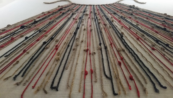 Photo (prise de biais) d'un quipu conservé au musée du Machu Picchu, trouvé sur la page Wikipédia qui leur est dédiée. L'objet est posé à plat sur une surface claire et on peut voir qu'il est constitué d'une corde principale à laquelle sont accrochées un certain nombre de cordelettes plus fines, aux couleurs variées, et qui présentent un certain nombre de nœuds. C'est apparemment la position de ces nœuds qui servait à transcrire l'information.