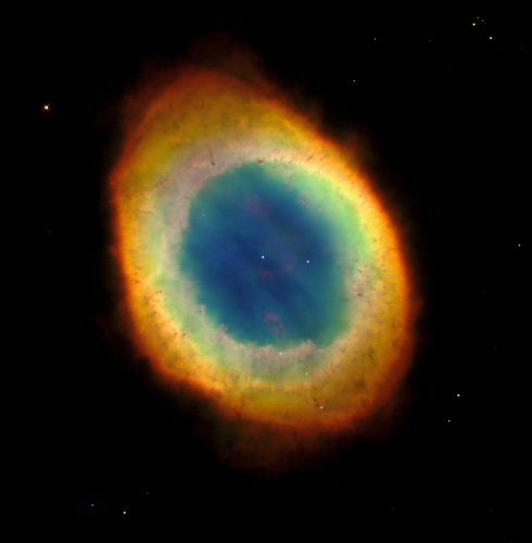 Photo (encore prise par le télescope spatial Hubble) de la nébuleuse de la Lyre, montrant des couches de gaz jaune-oranger sur l'extérieur, puis une partie tirant davantage vers le bleu au centre. Sur cette version (ça dépend beaucoup des photos), une seule étoile ressort par transparence à travers la partie centrale, et on repère plutôt bien la naine blanche au centre.