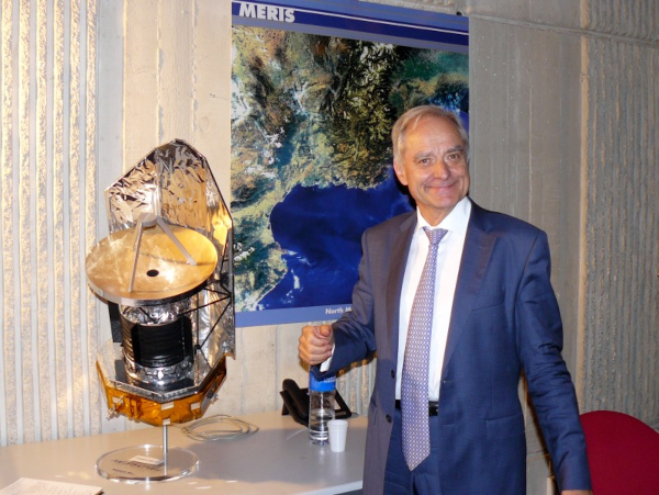 Photo trouvée sur Wikimédia Commons d'André Brahic, à qui est dédié ce thread, lors d'une conférence en 2009 dans l'auditorium du Thales Alenia Space à Cannes, où il était venu parler des satellites Herschel et Planck qu'il a contribué à lancer. L'homme est en costume bleu avec une longue cravate, avec des cheveux blancs et un large sourire. Une reproduction d'un des satellites est posée à côté de lui, et on peut voir une image satellite du sud de la France accrochée au mur derrière lui. Une version recadrée de cette image où l'on ne voit que l'astrophysicien illustre actuellement la page Wikipédia qui lui est dédiée.