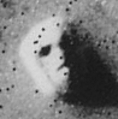 Photographie, trouvée sur Wikimédia Commons, du « Visage de Mars », recadrée pour centrer sur ce qui a attiré l'attention. On voit donc le sol martien vu de son ciel, avec tout un tas d'ombres noires à sa surface, mais surtout, au centre de l'image, un relief ressemblant à un visage humain dont la moitié gauche (la sienne, donc à droite pour nous) serait plongée dans l'ombre. En tout cas, les jeux d'ombres à la surface de ce relief semblent dessiner les formes de deux yeux, d'un nez, et d'une bouche.