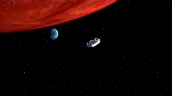 Image des environs de Yavin dans le premier film : on voit un morceau de la planète géante en haut à gauche, planète qui semble dominée par des tons rougeâtres, avec juste en dessous une petite lune plutôt bleue, avec quelques nuages visibles, le Faucon Millénium étant en train de voler dans la direction de cette lune. Je n'ai pas fait de calcul, mais à vue de nez comme ça, je pense que les proportions ne sont pas réalistes, j'ai plus l'impression de voir ce que ça donne quand je zoome les objets dans mon planétarium pour que les gens arrivent à les visualiser, mais il est éventuellement possible qu'un angle particulier donne quelque chose comme ça. On notera que le nom de la lune, Yavin Ⅳ, semble suivre la convention de nommage officielle chez nous : le nom de la planète suivi d'un numéro indiquant, selon le cas, l'ordre de proximité à la planète, ou celui de découverte. Il y a donc probablement ici au moins trois autres lunes, même si je ne me rappelle pas qu'elles aient été évoquées.