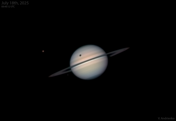 Photo, trouvée sur Wikimédia Commons, de Saturne sur laquelle est en train de passer l'ombre de Titan. Le satellite naturel lui-même est visible sur la gauche, et on voit, environ au milieu de la partie de Saturne située au dessus des anneaux, un gros point noir, correspondant à la partie de la géante gazeuse qui n'est pas éclairée parce que Titan lui masque la partie du Soleil, causant donc une éclipse.