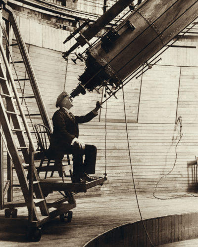 Photo de Percival Lowell dans son observatoire (la légende de l'image dit qu'il était pour le coup en train d'observer Vénus), trouvée sur la page Wikipédia consacrée au bonhomme. On le voit assis sur une chaise qui semble fixée sur une échelle et pouvant donc monter et descendre, et en train de mettre son œil sur l'objectif d'un télescope assez gros pour qu'il puisse y entrer tout entier. Cette image apparaît d'ailleurs brièvement dans ma vidéo sur Pluton, car la découverte d'une neuvième planète était l'autre marotte de Lowell, et c'est au sein de son observatoire que Clyde Tombaugh découvrira plus tard ce que l'on considère aujourd'hui comme une planète naine.