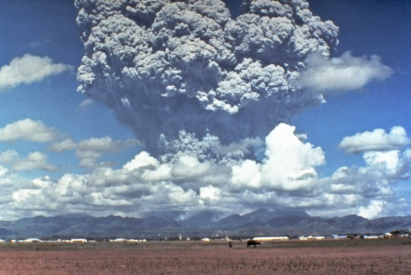 Photo d'un panache volcanique trouvée sur la page Wikipédia qui leur est dédiée, et qui provient de l'éruption du Pinatubo aux Philippines en 1991. On voit des champs en bas avec une chaîne de montagne dans le lointain, et en haut, un gigantesque nuage de gaz qui semble s'élever à plusieurs kilomètres d'altitude.