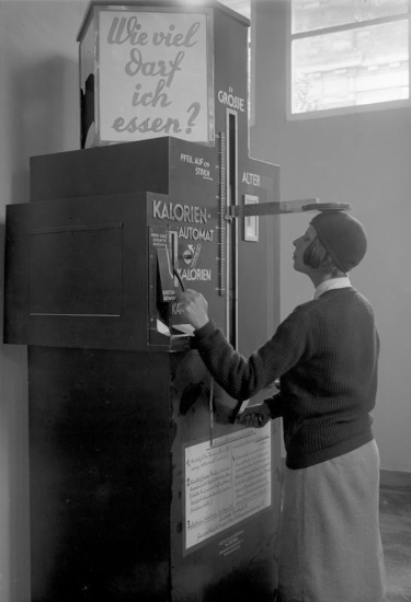 Parce que je ne savais pas trop comment illustrer ce pouet, voici une photo qu'on trouve actuellement sur la page Wikipédia francophone dédiée aux calories. On y voit une machine avec des écriteaux en allemand, devant laquelle une personne est en train de se faire mesurer : la machine servait à estimer, en fonction de sa taille et de son poids, combien de calories la personne était censée consommer.