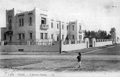 Photo, prise en 1900 et trouvée sur la page Wikipédia dédiée, de l'Institut Pasteur… non pas à Paris, mais à Tunis. Dès le départ, cet établissement était en effet international, avec des bâtiments dans plusieurs villes de France (Lille en particulier) et dans plusieurs pays du monde (en Afrique et en Asie du sud-est notamment). On voit globalement sur l'image, qui est en noir et blanc vu l'époque, un grand bâtiment avec une personne qui l'observe depuis la rue.
