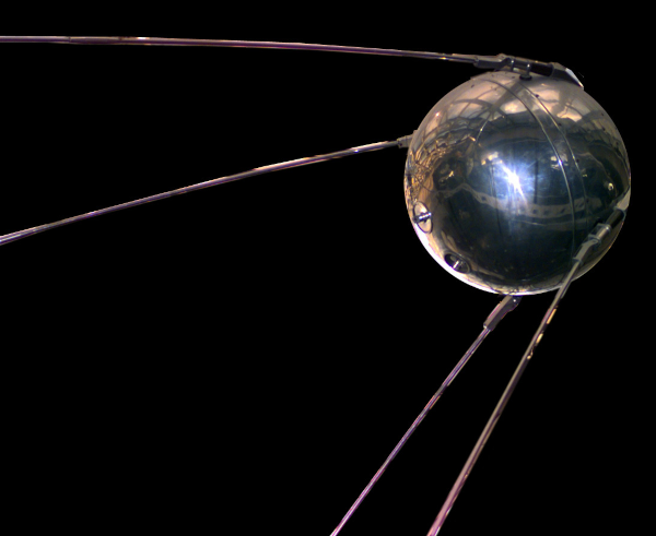 Photo d'une reconstitution du Spoutnik original, illustrant actuellement sa page Wikipédia. On voit, sur fond noir, une grosse boule métallique avec quatre antennes sur les côtés et qui partent vers l'arrière. 