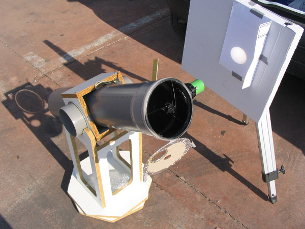 Photo, trouvée sur Wikimédia Commons, d'un dispositif de projection pour observer le Soleil, comme ce dont on a parlé au pouet précédent. On voit un télescope posé sur un support fait maison, avec un panneau posé sur un trépied en face de son objectif. Au lieu de regarder dans ce dernier, on va donc observer l'image du Soleil qu'il projette sur le panneau. On repère ici un cercle lumineux, sans aucune activité particulière, mais ce type de dispositifs permet d'admirer les taches solaires quand il y en a… et bien sûr les éclipses.