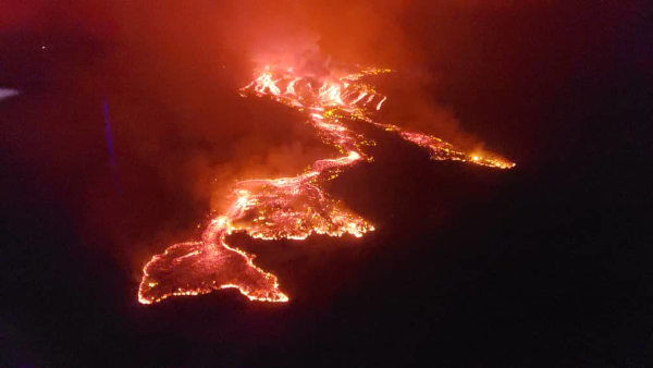 Photo (trouvée sur Wikipédia) de l'éruption du Nyiragongo en 2021, typiquement effusive. L'image est assez sombre avec de la fumée qui empêche de voir beaucoup de détails, mais on voit nettement la lave rouge qui s'écoule depuis le volcan situé à l'arrière-plan et avance vers le bas de l'image.