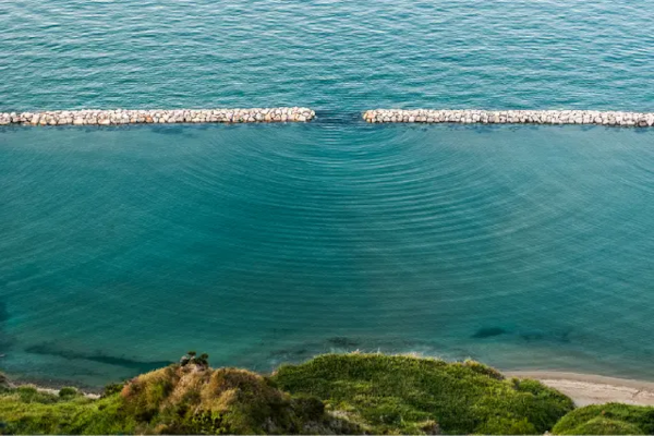 Photographie trouvée sur Internet montrant un mur avec une ouverture (une seule visible, malheureusement) dans une étendue d'eau, montrant les vagues qui se forment d'un côté de façon concentrique, comme sur le schéma du premier pouet, parce que jusque là l'expérience peut être réalisée avec n'importe quel type d'onde. On repère d'ailleurs sur le côté d'autres diffusions montrant des interférences, signe qu'il y a bien plusieurs fentes dans le mur, elles sont seulement hors de vue.