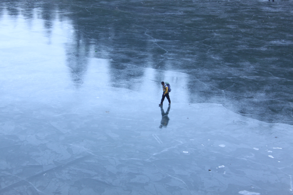 Photo d'un lac gelé (prise apparemment au Kosovo) sur lequel on voit des ombres se refléter. Une personne est en train de marcher sur la glace au milieu de l'image.