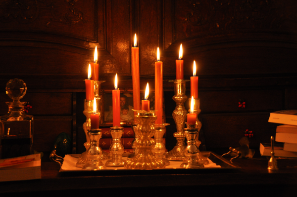Photo, illustrant actuellement la page Wikipédia sur les bougies, de plusieurs d'entre elles allumées et posées sur de petits chandeliers, posées devant ce qui ressemble à une porte de placard (une photo montrant des gens peut être devinée à l'arrière-plan) et quelques objets, dont des livres, sont posés autour.