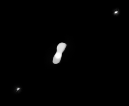 Photographie de l'astéroïde (216) Cléopâtre prise par le VLT. On voit sa forme plus ou moins allongée, sur fond noir. De chaque côté du satellite, une tache blanche un peu floue indique la présence d'un de ses compagnons, deux astéroïdes plus petits et moins allongés qui lui tournent autour.