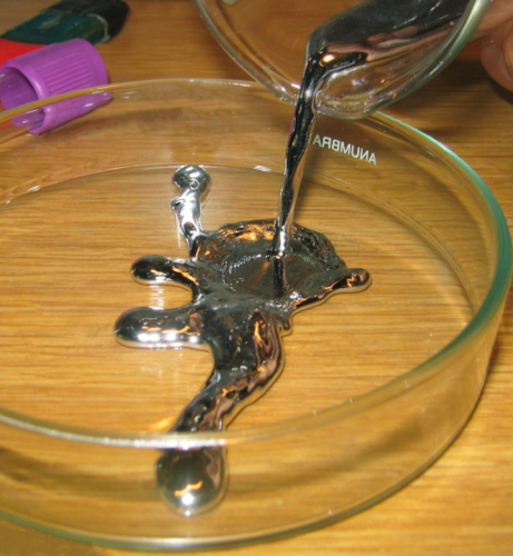 Photo, trouvée sur la page Wikipédia dédiée à ce liquide, de mercure en train d'être versé d'un récipient vers un autre (en l'occurence, ça me semble être un bécher et une boîte de Pétri). On voit donc un liquide opaque et à l'aspect métallique (normal, le mercure est un métal, même s'il est le seul métal liquide à température et pression ambiantes) couler depuis l'un des deux récipents pour s'étaler dans l'autre, partant dans diverses direction, un peu comme l'eau quand on la verse. Le mercure est un liquide plus dense que l'eau, et potentiellement dangereux pour la santé, mais ça reste un liquide, qui se comporte comme un liquide, donc.