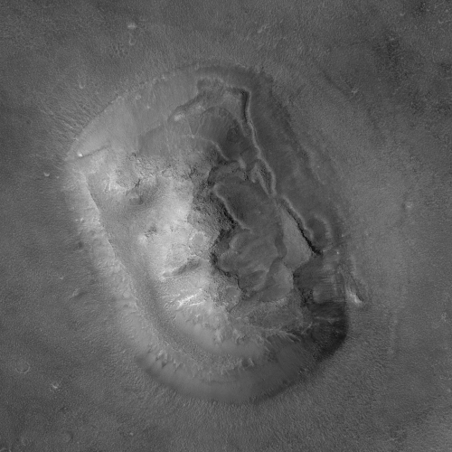 Photo de Cydonia Mensae prise par la sonde Mars Global Surveyor, et trouvée sur la page Wikipédia qui est dédiée à l'endroit, où il y en a d'ailleurs quelques autres assez intéressantes. On voit globalement la même forme générale du relief, mais les ombres étant très différentes, l'impression de voir un visage disparaît totalement (à la limite, celle-ci m'évoquerait peut-être plus un bouclier). En prêtant attention, on repère quand même à peu près les creux et bosses qui ont donné l'impression, sur l'image de Viking 1, de voir des yeux, un nez et une bouche, mais c'était très clairement une simple impression.