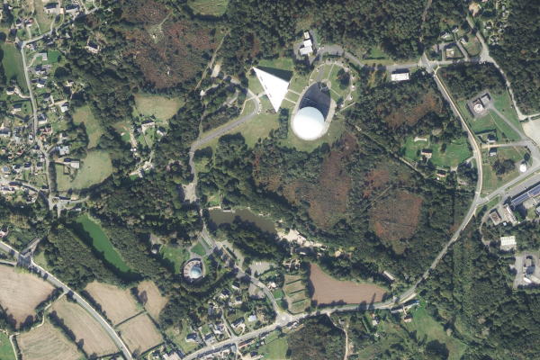 Photographie aérienne du parc du Radôme à Pleumeur-Bodou, trouvée sur Internet. On voit une zone majoritairement boisée avec des routes un peu tout autour et un certain nombre de maisons, principalement à gauche et en bas. Le Radôme est la grosse boule blanche vers le milieu-haut de l'image, avec d'autres bâtiments autour, formant la Cité des Télécoms. Plus bas se trouve une boule plus petite avec le reste du bâtiment en forme de demi-cercle autour : c'est le Planétarium de Bretagne. Entre les deux (du côté du plané) se trouve un petit lac, qui fait partie du Village Gaulois.