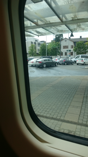 Photo, trouvée sur Wikimédia Commons, de la vue depuis la fenêtre d'un train, en l'occurrence vers ce qui doit être le parking de la gare puisqu'on voit plusieurs voitures stationnées. Il vous est peut-être déjà arrivé, au départ d'un train, de regarder vers la fenêtre et d'avoir l'impression que c'est la gare qui se mettait à bouger. Ce n'est pas qu'une impression : les cahots et vibrations nous indiquent que c'est bien nous qui bougeons, mais si nous pouvions les supprimer complètement, nous n'aurions simplement aucun indice nous permettant de déterminer si c'est le train ou l'extérieur qui se déplacent. Les deux reviennent en fait la plupart du temps strictement au même.