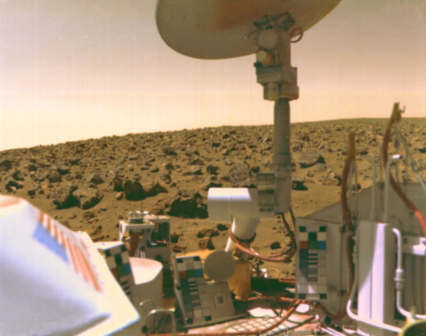 Photo du site d'atterrissage de Viking 2, prise par la sonde le 3 septembre 1976 et trouvée sur la page wikipédia qui lui est dédiée. On voit le ciel aux couleurs maronnasses de Mars en haut, plus bas un terrain constitué uniquement de sable et de cailloux, et au premier plan, quelques uns des équipements du robot qui ont servi à faire les expériences que je décris ici, et, remontant jusqu'en haut de l'image, une antenne parabolique. En fait, cette antenne ne servait qu'à communiquer avec la deuxième partie du robot, restée en orbite et qui servait à relayer les communications vers la Terre, en plus d'occasionnellement photographier des visages dans les rochers comme on en parlait la semaine dernière.