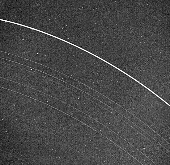 Photo des anneaux d'Uranus prise par la sonde Voyager 2, et trouvée sur Wikipédia. On voit globalement une série de neuf cercles (si je recompte bien, les plus fins sont un peu noyés dans le bruit de fond de l'image) avec quelques étoiles en arrière-plan. L'anneau le plus extérieur est beaucoup plus épais, et les autres sont d'épaisseur variable, la quantité de matière présente dans ces anneaux n'étant pas toujours la même. (Toutes les photos de Voyager 2 montrées ici sont en noir et blanc.)