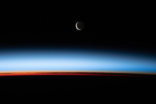 Et pour finir, une photo de la Terre prise depuis l'ISS. La photo est prise de nuit et on ne voit pas les continents, mais on distingue l'atmosphère colorée et un croissant de Lune dans le ciel… à sa taille habituelle, puisque, quatre milliards et demi d'années plus tard, elle a eu le temps de reculer un peu. Aux échelles de temps que prend tout ça, nous sommes figés sur un instantané, mais la Terre continuera de changer dans le futur.